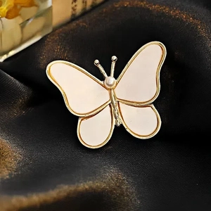 Close-up of golden butterfly brooch with cream inlay and pearl on black silk fabric