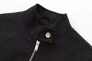 Detail of black twill jacket featuring a stand collar, silver zipper and metal button