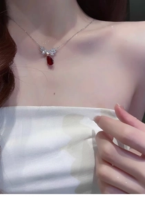 Close-up of a silver necklace with a red teardrop zircon pendant on a woman's neck
