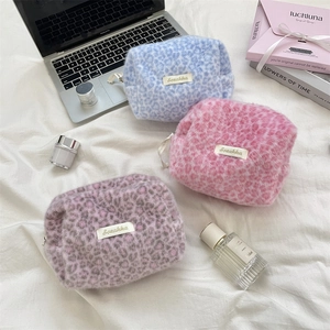 Three plush leopard print makeup bags in blue, pink, and purple with gold logo labels