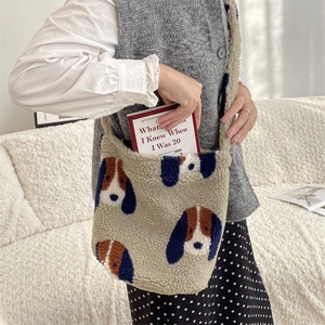Close-up of beige plush tote bag with blue dog pattern holding a book on a cozy sofa