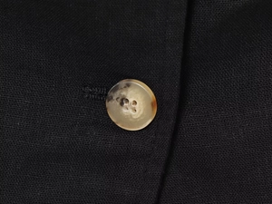 Detailed close-up of amber button and black linen blend fabric on a double-breasted vest