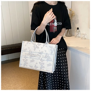 Silver tote bag with butterfly embroidery held by a model in a casual outfit