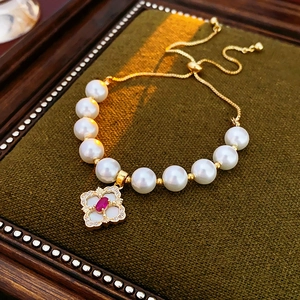 Detail of gold pearl bracelet with clover pendant on green velvet display pad