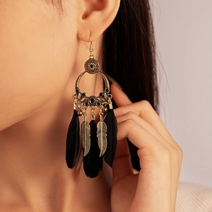Detail of bohemian gold hollow hoop earrings with black feathers on model