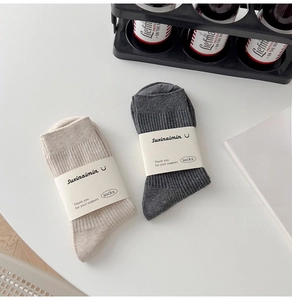 Detail of cream and dark grey ribbed crew socks with paper packaging on white surface