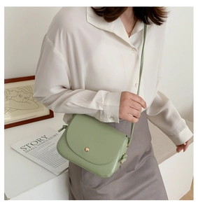 Close-up of light green crossbody bag with a round metallic magnetic clasp on a model