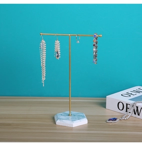 Detailed view of golden T-bar jewelry stand with hexagonal marble base on a wooden desk