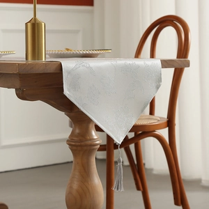 Silver damask table runner with decorative tassel on wooden dining table setting
