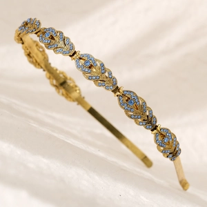 Detail of golden wheat leaf headband featuring blue rhinestones on textured white fabric