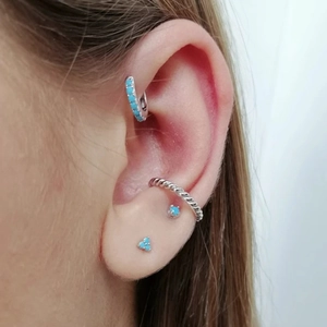 Detail of silver floral earrings set with turquoise stones worn on ear cartilage