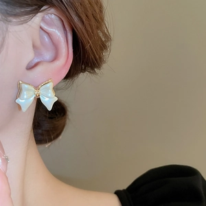 Close-up of elegant bow-shaped pearl stud earrings with gold trim worn by a model