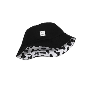 Reversible bucket hat with cow print lining and black exterior featuring a smiley face patch