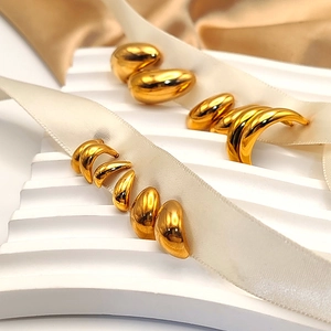 Detail of 18K gold teardrop and crescent earrings on elegant white ribbon display