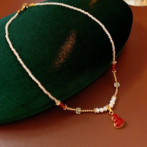 Macro detail of red gourd pendant on freshwater pearl necklace with gold accents