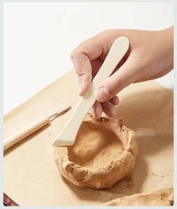 Close-up of a hand using wooden pottery tools to shape a clay bowl on kraft paper