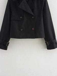 Détail d'un trench-coat court noir à double boutonnage avec boutons et brides de poignets