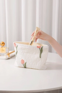 Detail of white crepe cosmetic bag with elegant tulip embroidery and soft wrinkled texture