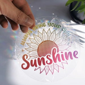 Close-up of a round holographic suncatcher sticker with Always Bring Your Own Sunshine text