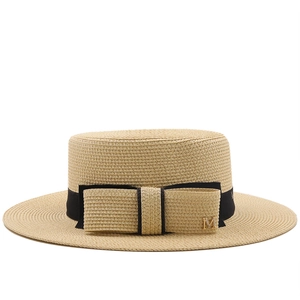 Close-up of beige straw boater hat with black ribbon and gold M letter metal detail
