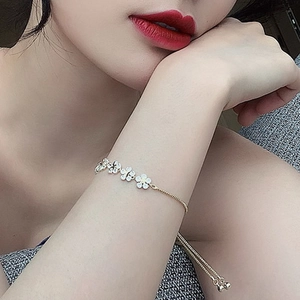 Close-up of a gold adjustable flower bracelet with white enamel on a model wrist