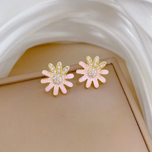 Close-up of gold daisy earrings with pink enamel petals and sparkling crystal center