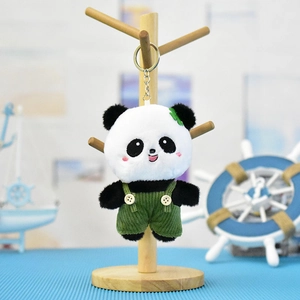 Schattige panda pluche sleutelhanger met groene overall aan een houten displaystandaard