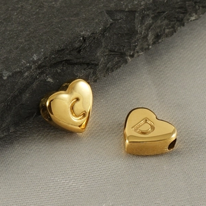 Macro view of gold heart-shaped charms with engraved letters C and D for DIY jewelry