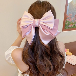 Detail of a large pink satin bow hair clip worn by a model in a French elegant style