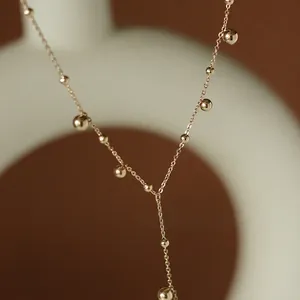 Y-shaped gold ball tassel necklace in 18K gold plated stainless steel on beige background