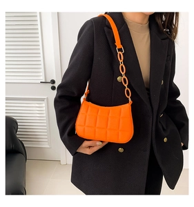 Detail der orangefarbenen Stepptasche mit schicker Kette auf schwarzem Blazer