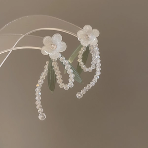 Close-up of white matte floral earrings with transparent crystal bead fringe detail