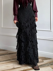 Detail of black maxi skirt featuring white polka dots and elegant side ruffle decoration