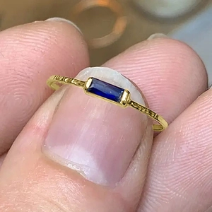 Detail of a thin gold band ring featuring a rectangle blue stone and hammered texture