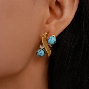 Close-up of gold earrings with turquoise beads and rhinestones worn by a model