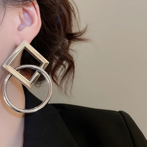 Close-up of interlocking square and round silver earrings worn by a model in black suit