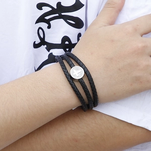 Macro detail of triple-layer braided leather bracelet featuring a metal cross charm