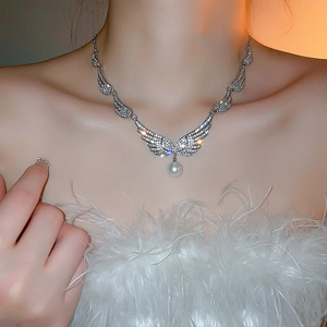 Detail of angel wing necklace with cubic zirconia and pearl on female model