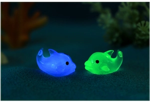 Close-up of blue and green glowing resin dolphin figurines in a dark aquarium setting