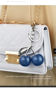 Blue glitter resin cherry pendant accessory shown on a white quilted chain bag