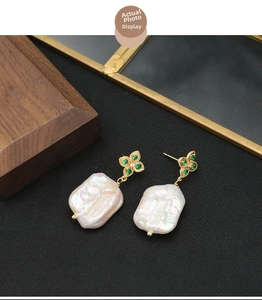 Detailed view of baroque pearl earrings with golden flower studs on a dark background