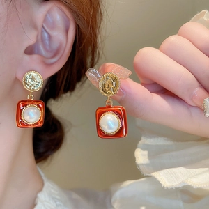 Gros plan d'une boucle d'oreille en pièce d'or vintage avec cadre émail rouge et perle