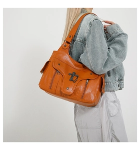 Detail der orangefarbenen PU-Schultertasche mit Metallkreuz-Anhänger und Reißverschlusstaschen