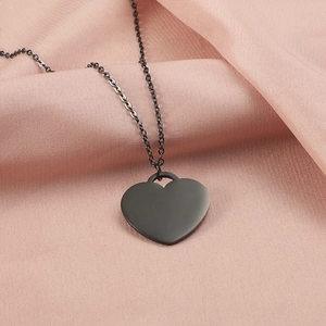 Flat lay of a matte black heart pendant necklace on soft pink textured fabric backdrop