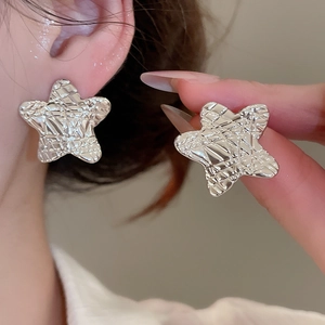 Detailed view of silver star earrings with hammered texture on earlobe and fingertip