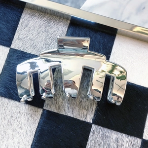 Metallic silver shark hair claw clip on checkerboard background in minimalist style