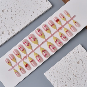Pink French press-on nails set with 3D cherry patterns and red bows on a white board