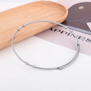 Detailed macro view of silver steel cable choker with metal beads on a wooden tray