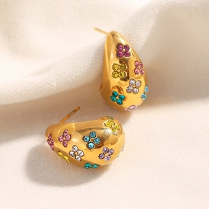 Detail of gold drop earrings with colorful clover pattern gemstones on beige fabric