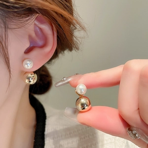 Elegant gold metal and white pearl dual-ball stud earrings shown on ear and in hand